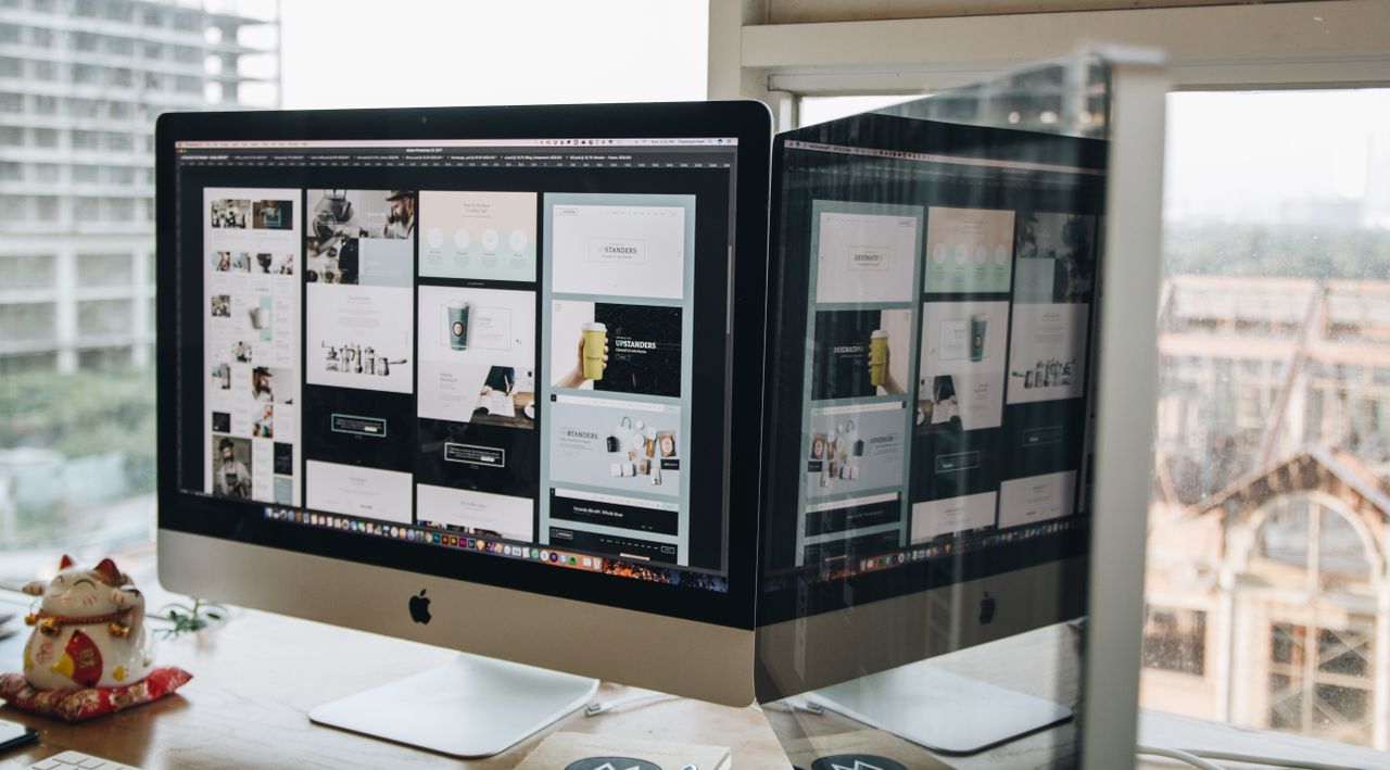 who-we-are Dual monitors on a desk, showcasing web design in a modern office setting.